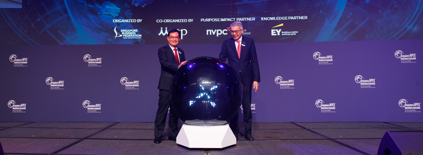 Two people in suits beside a glowing sphere on a stage in front of an event banner.